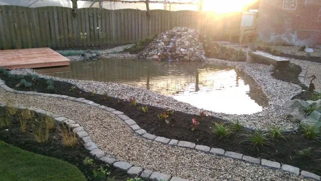 Aangelegde vijver met een stenen waterval, omzoomd door een grindpad met natuursteenband en verse beplanting