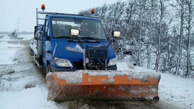 Bedrijfsbus met oranje sneeuwschuif en zwaailicht op een besneeuwde weg