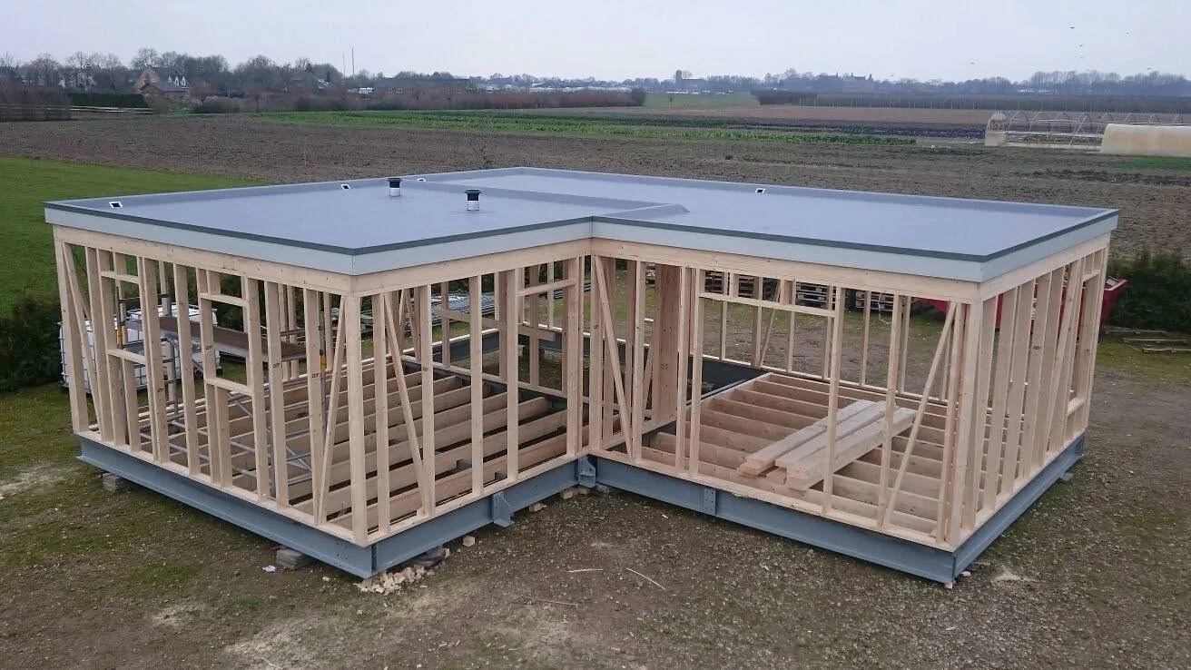 Mantelzorgwoning in aanbouw: een houten skeletbouw met plat dak, staand op een grijs stalen onderframe in het veld