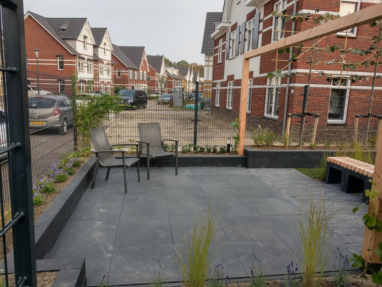 Stadstuin met een groot terras van donkere tegels, verhoogde borders met een zwarte band en een houten pergola