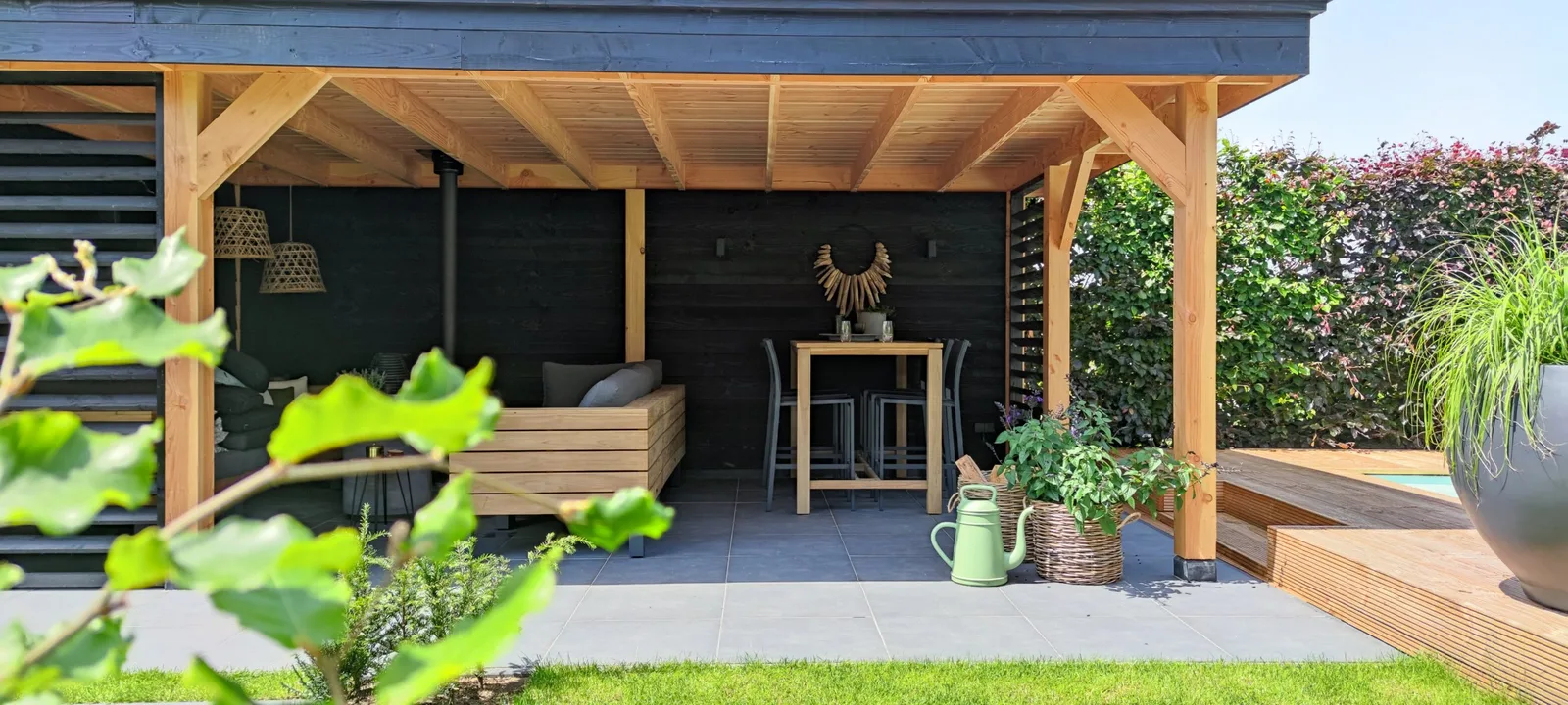Houten overkapping met loungeset en bar, naast een vlonder en een strak gazon